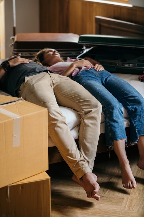 Tired couple lying on bed near boxes