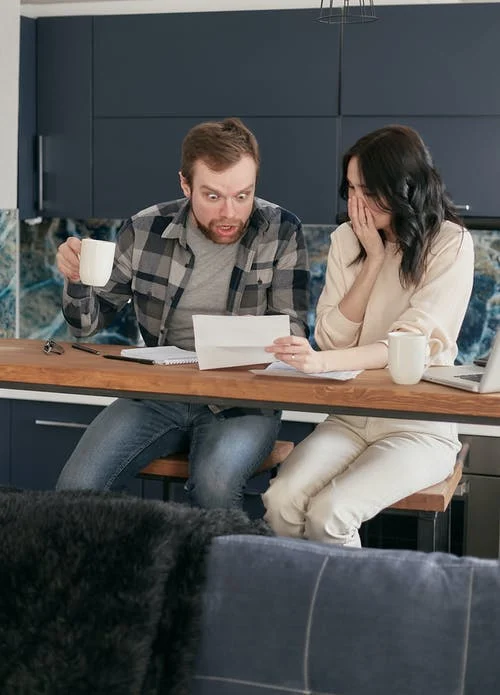 Couple Sitting Near the Wooden Table while Looking at the Document in Shocked Emotion