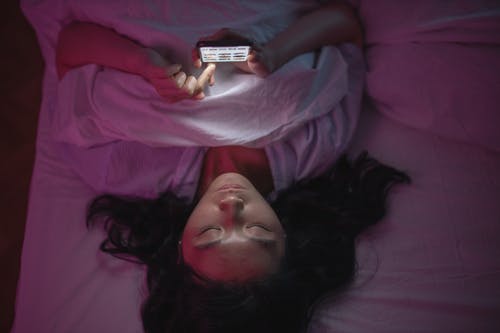 Woman Lying on Bed Holding Iphone