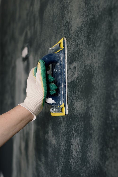 worker in gloves holding scraper and aligning walls in flat